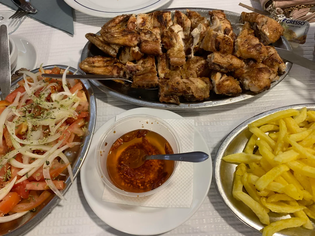Close-up of chargrilled piri piri chicken with crispy skin, served with golden fries and fresh tomato salad in a Portuguese restaurant